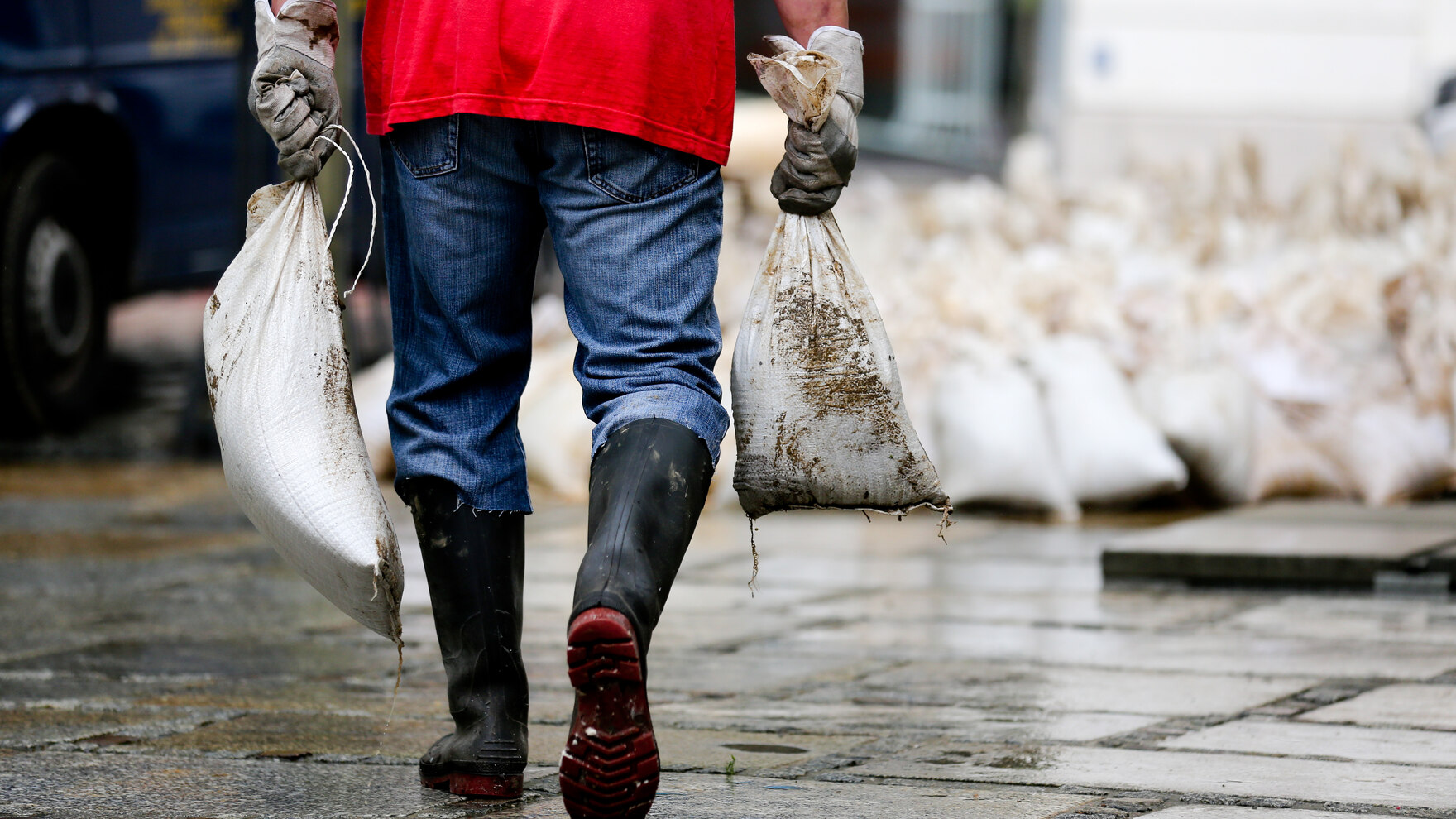Ein Helfer trägt Sandsäcke bei einem Hochwasser.