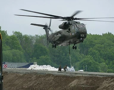 Ein Helikopter der Bundeswehr hilft Feuerwehrleuten beim Bau eines Schutzdamms gegen Hochwasser.