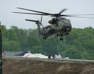 Ein Helikopter der Bundeswehr hilft Feuerwehrleuten beim Bau eines Schutzdamms gegen Hochwasser.
